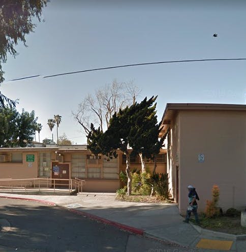 Building exterior with trees and a person walking on a sidewalk