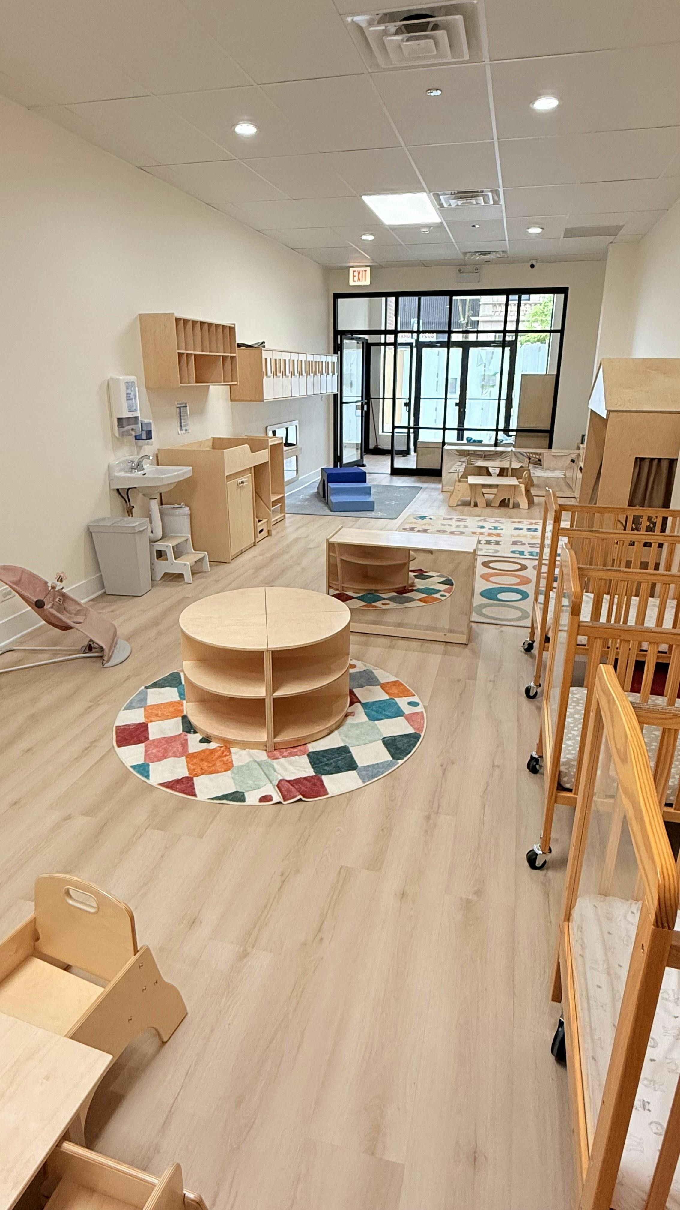 Daycare room with cribs, small tables, and play areas