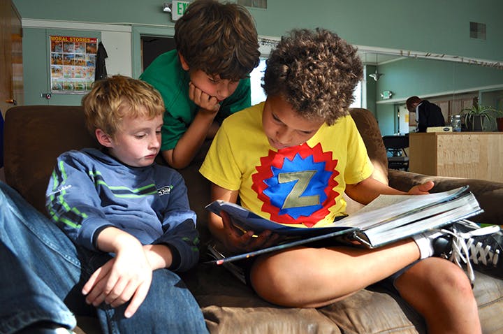 Three children sitting on a couch reading a book together
