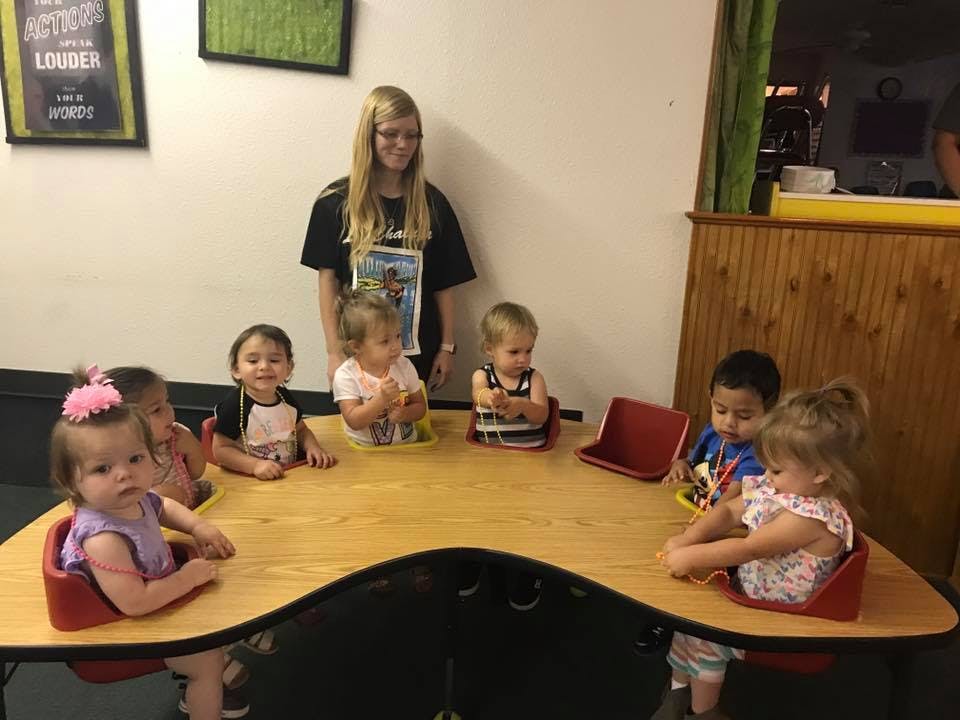 Person standing behind a table with multiple children seated