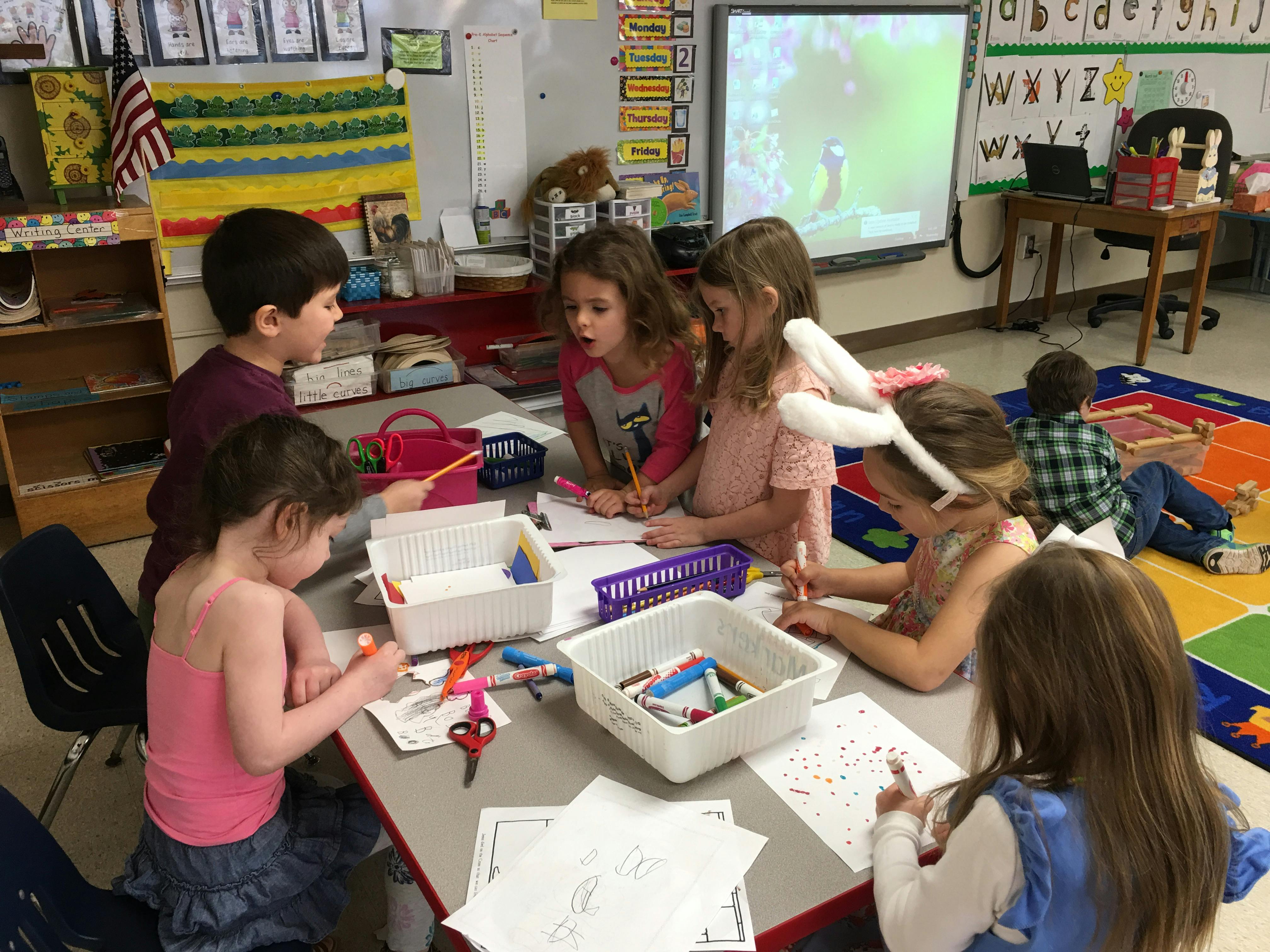 Children drawing and writing at a table in a classroom