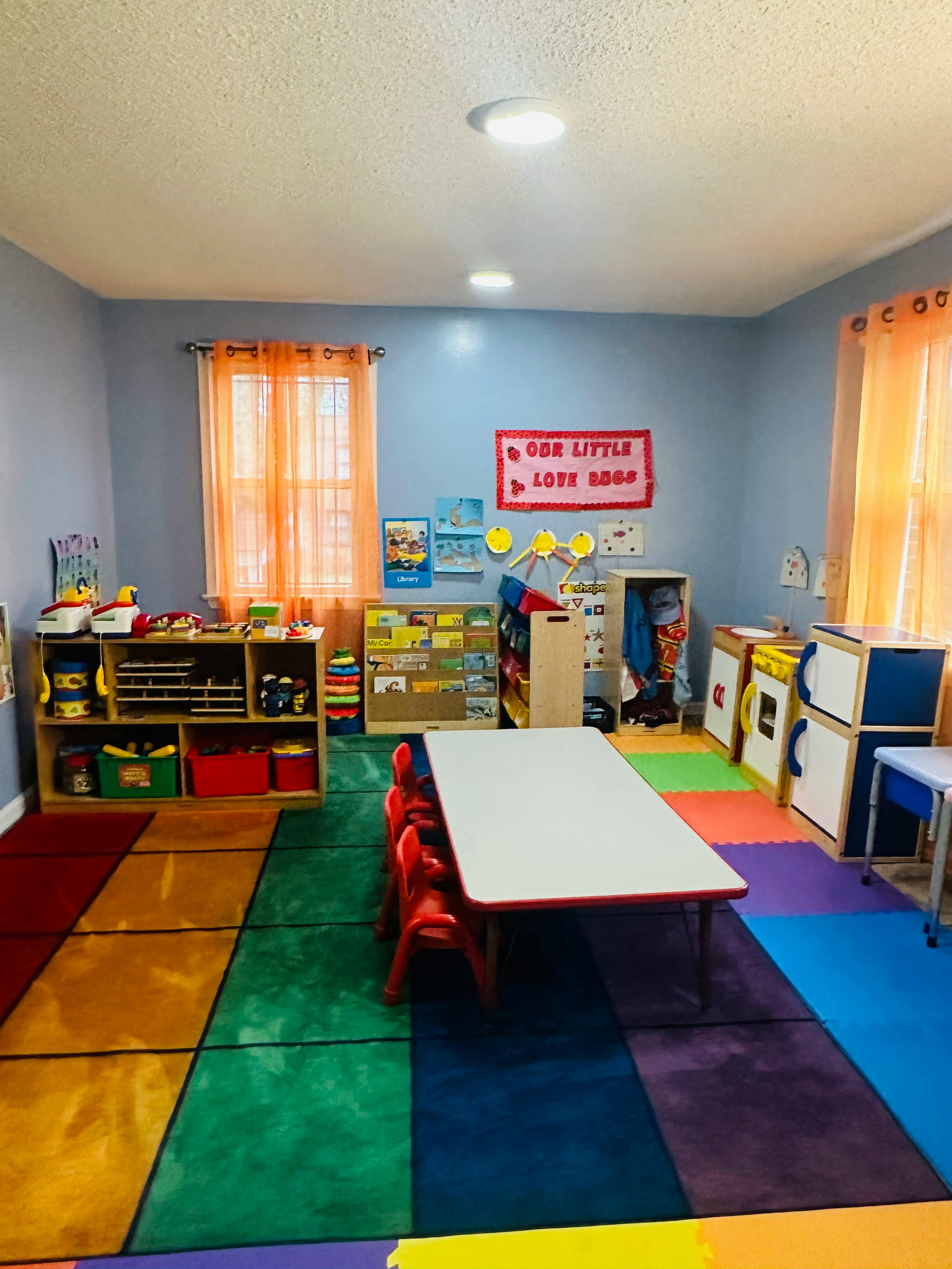 Classroom with colorful rug, small table and chairs, and shelves with toys