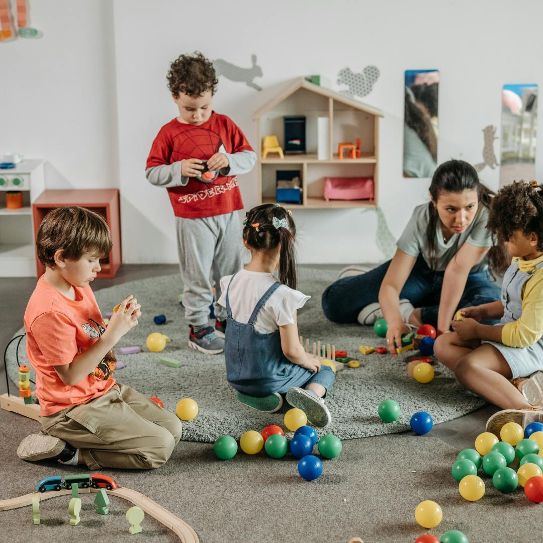 Adult and children playing with toys on the floor in a classroom