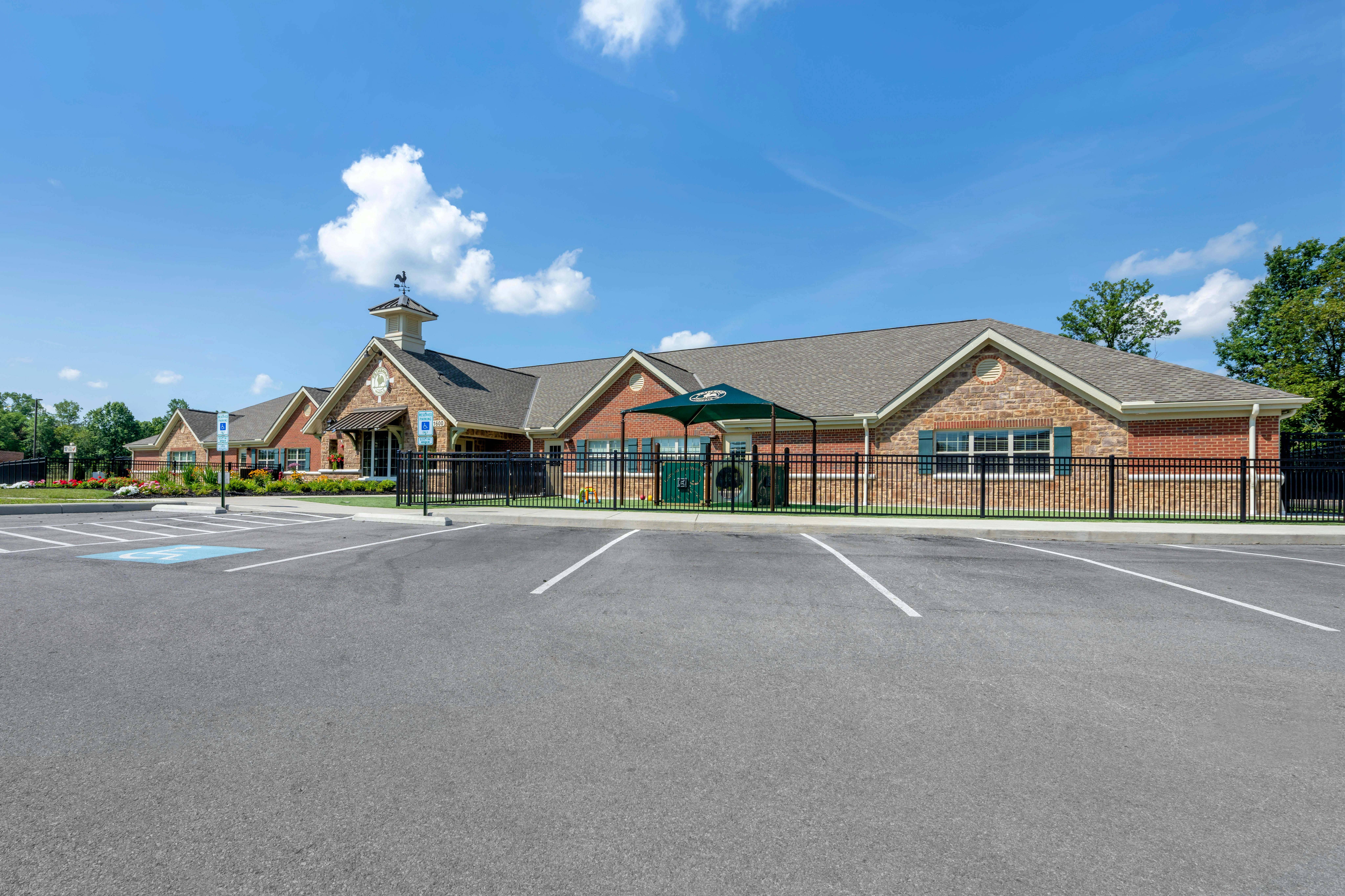 Parking lot in front of a brick building with a cupola and a fenced playground