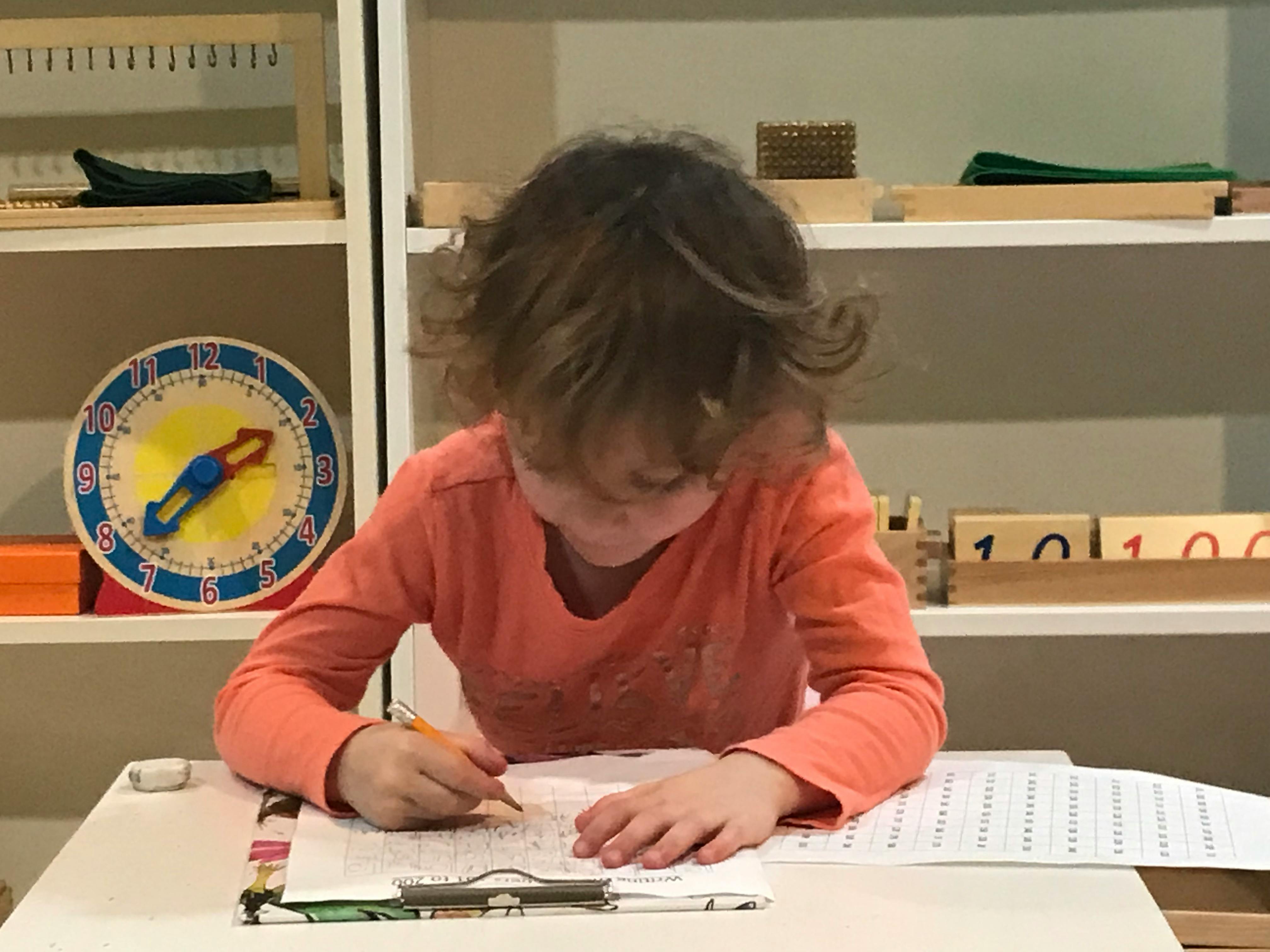 Child writing on paper at a desk in a classroom