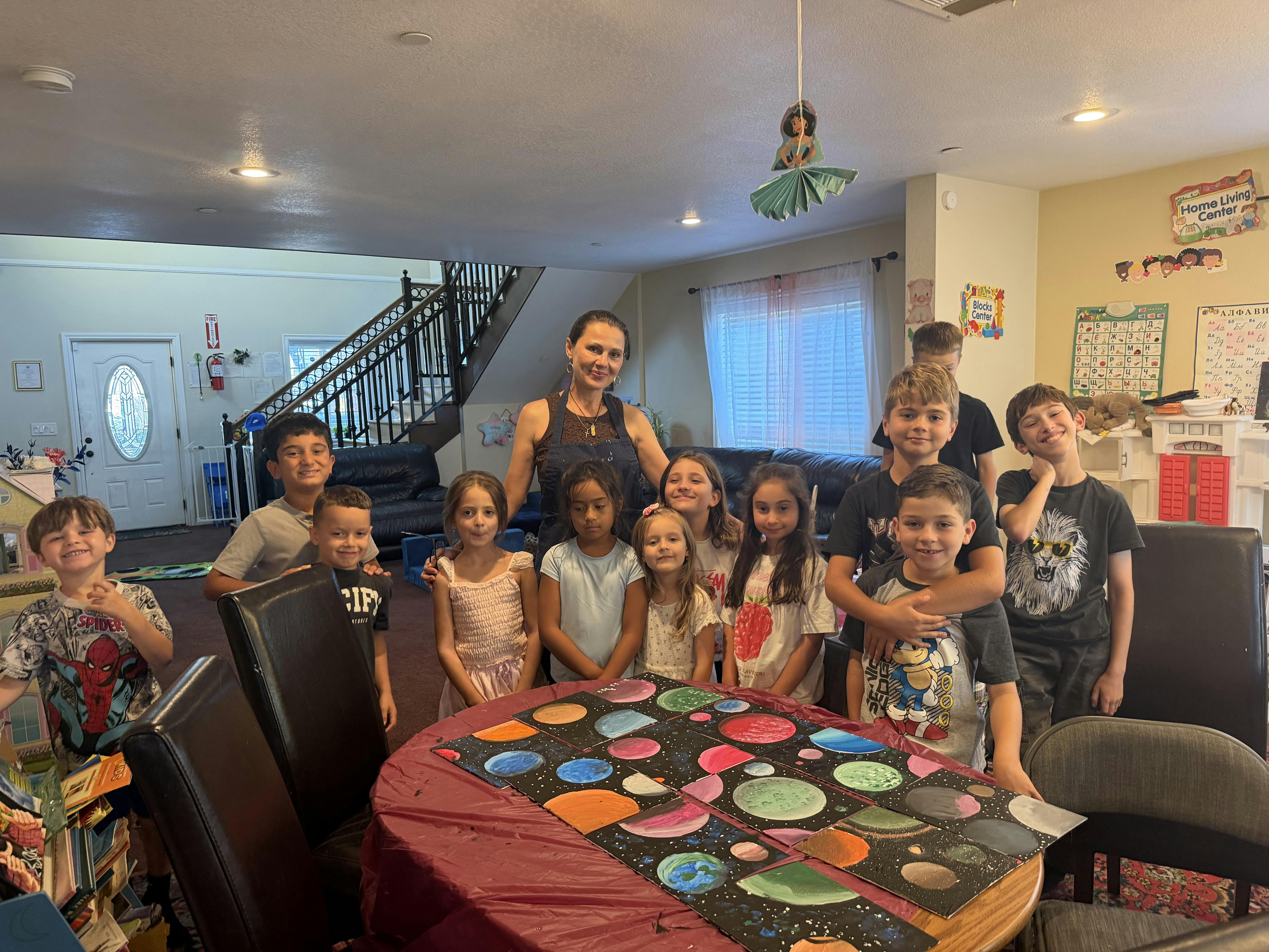 A person and children posing with paintings of planets at a table