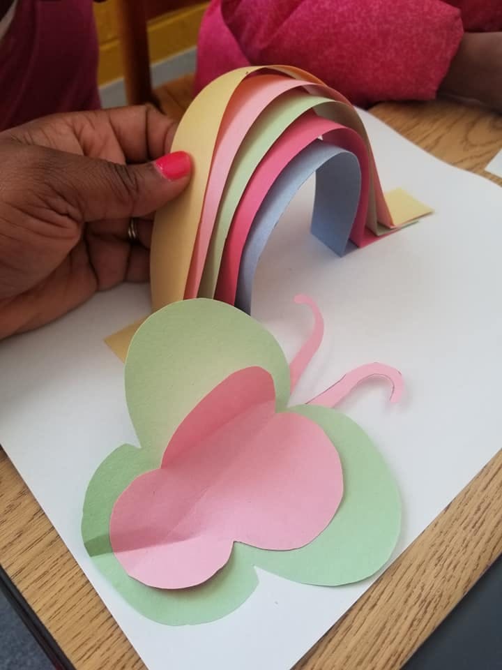 Person holding a paper rainbow craft next to a paper butterfly