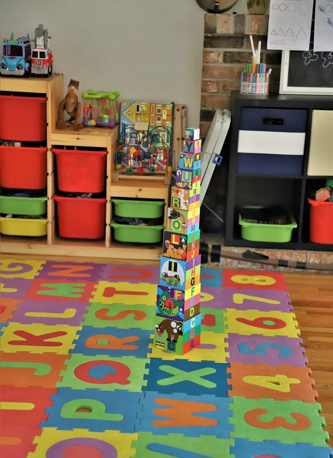Tall stack of colorful alphabet blocks on a playmat with letters and numbers