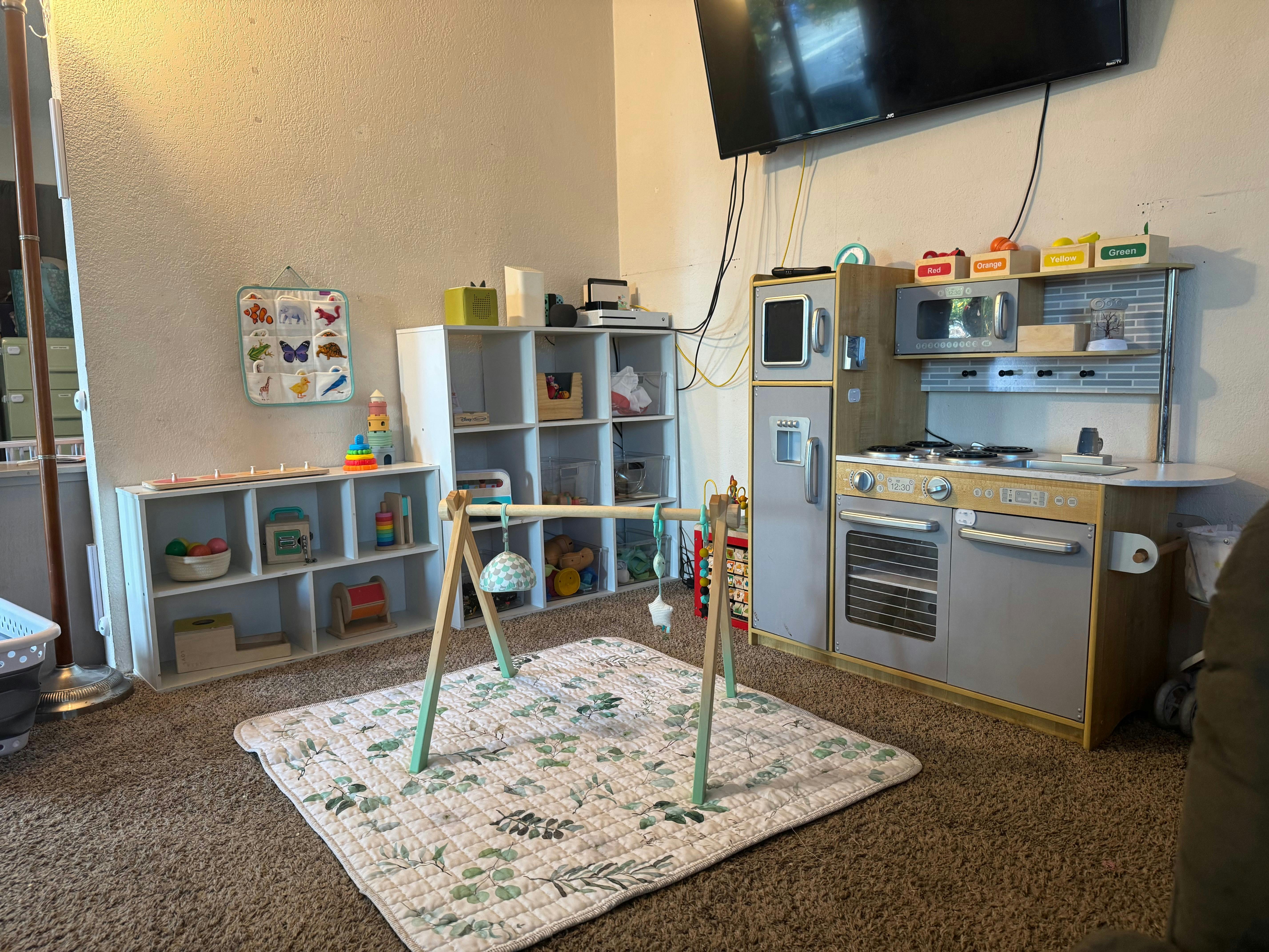 Child's play area with a play kitchen, toy shelves, and a baby gym on a mat
