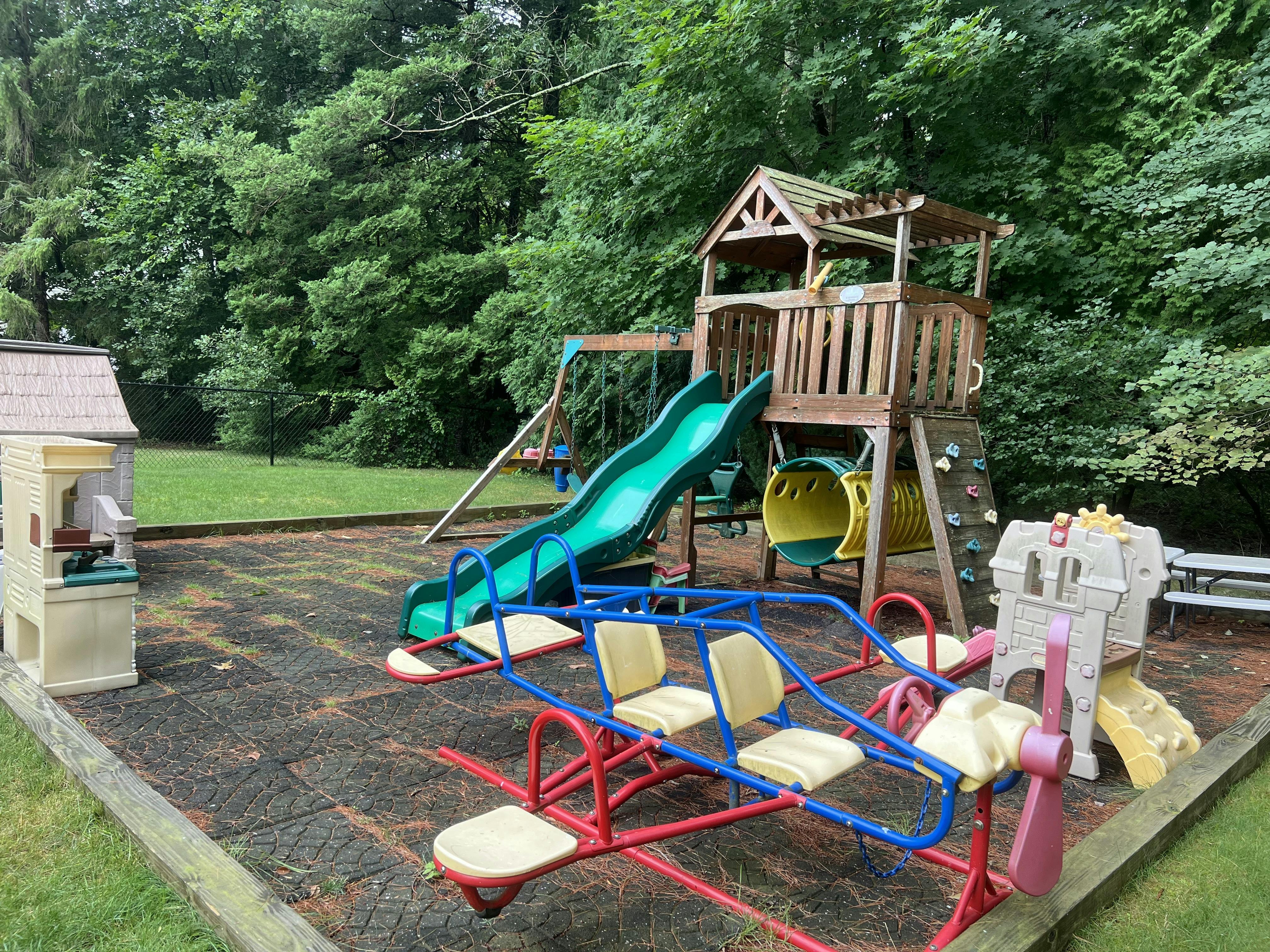 Outdoor playground with wooden playset, green slide, and seesaw