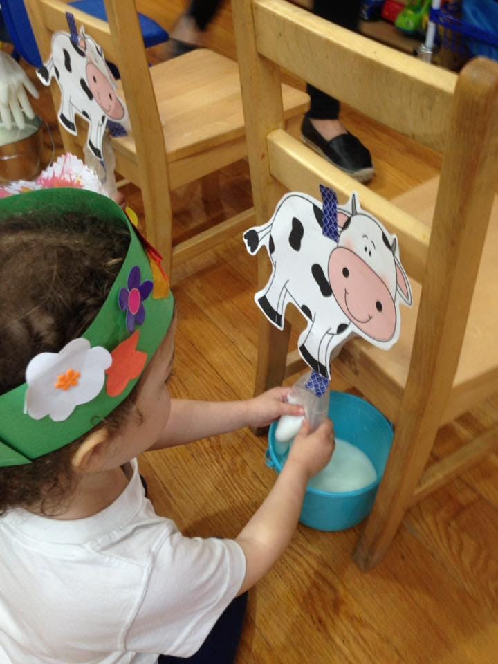 Child wearing a flower crown playing with a cow cutout and a bucket