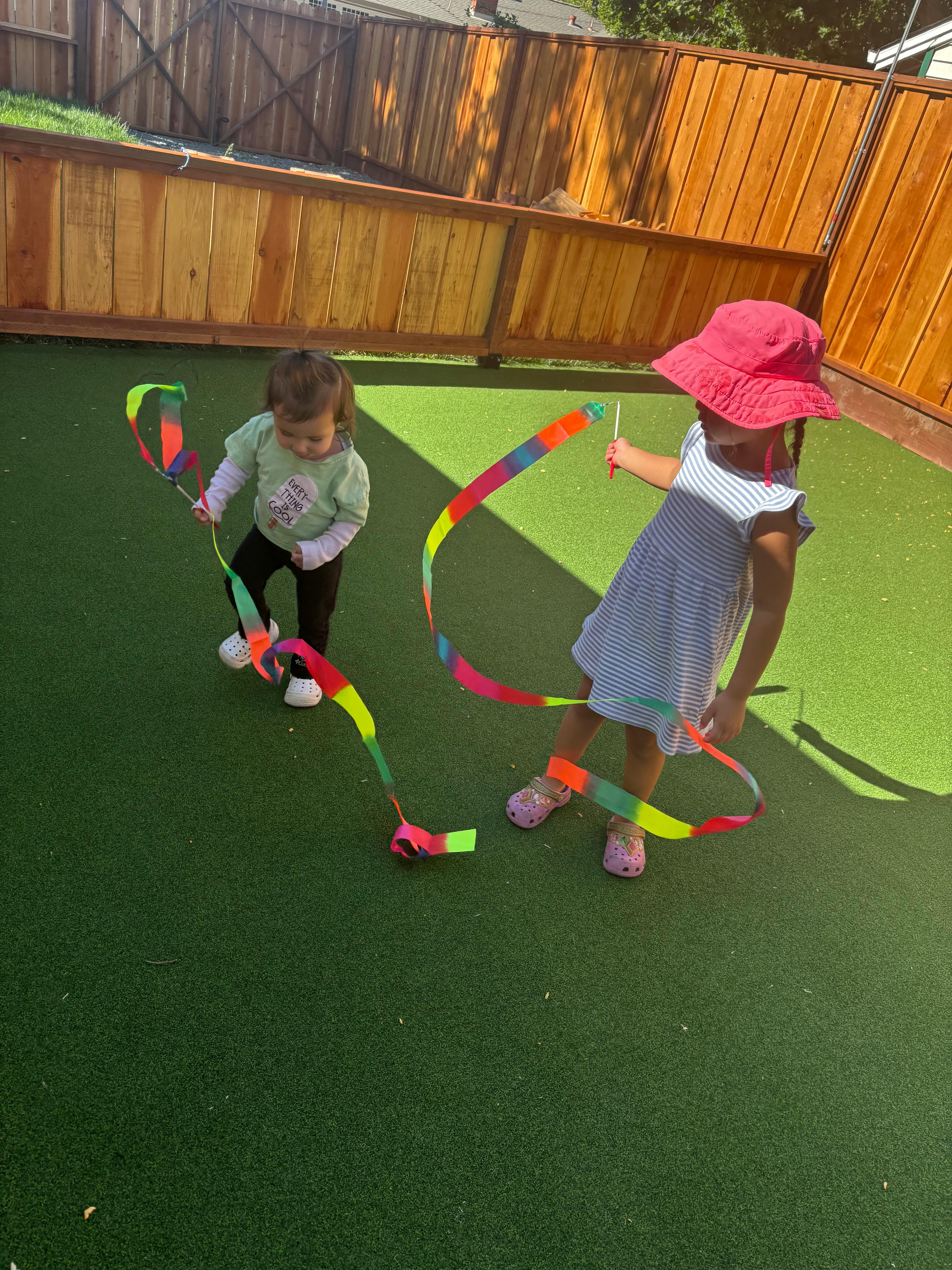 Two children playing with colorful ribbons on artificial turf