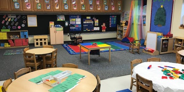 Classroom with small tables and chairs, colorful rug, and learning materials