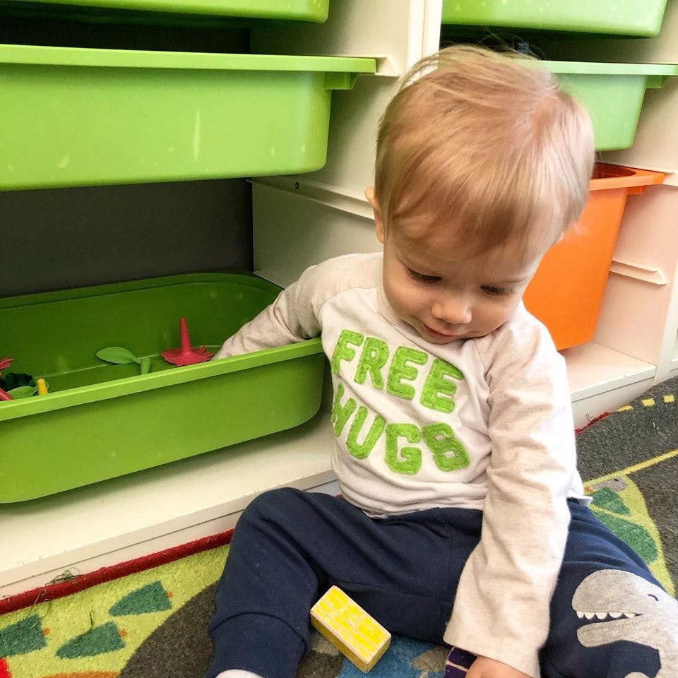 Child sitting on floor next to green bin with toys