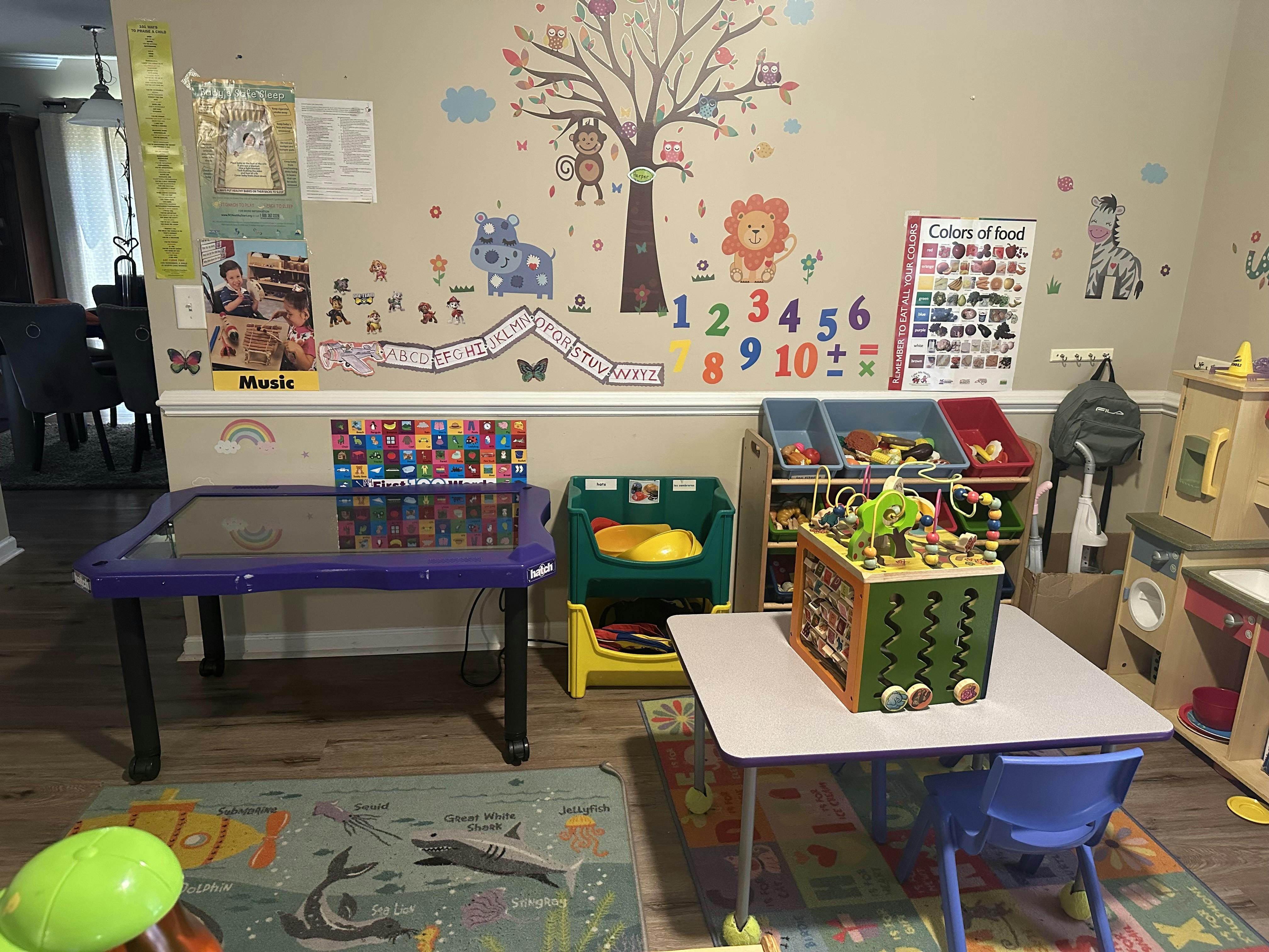 Playroom with tables, chairs, and toys, with wall decals of animals and numbers