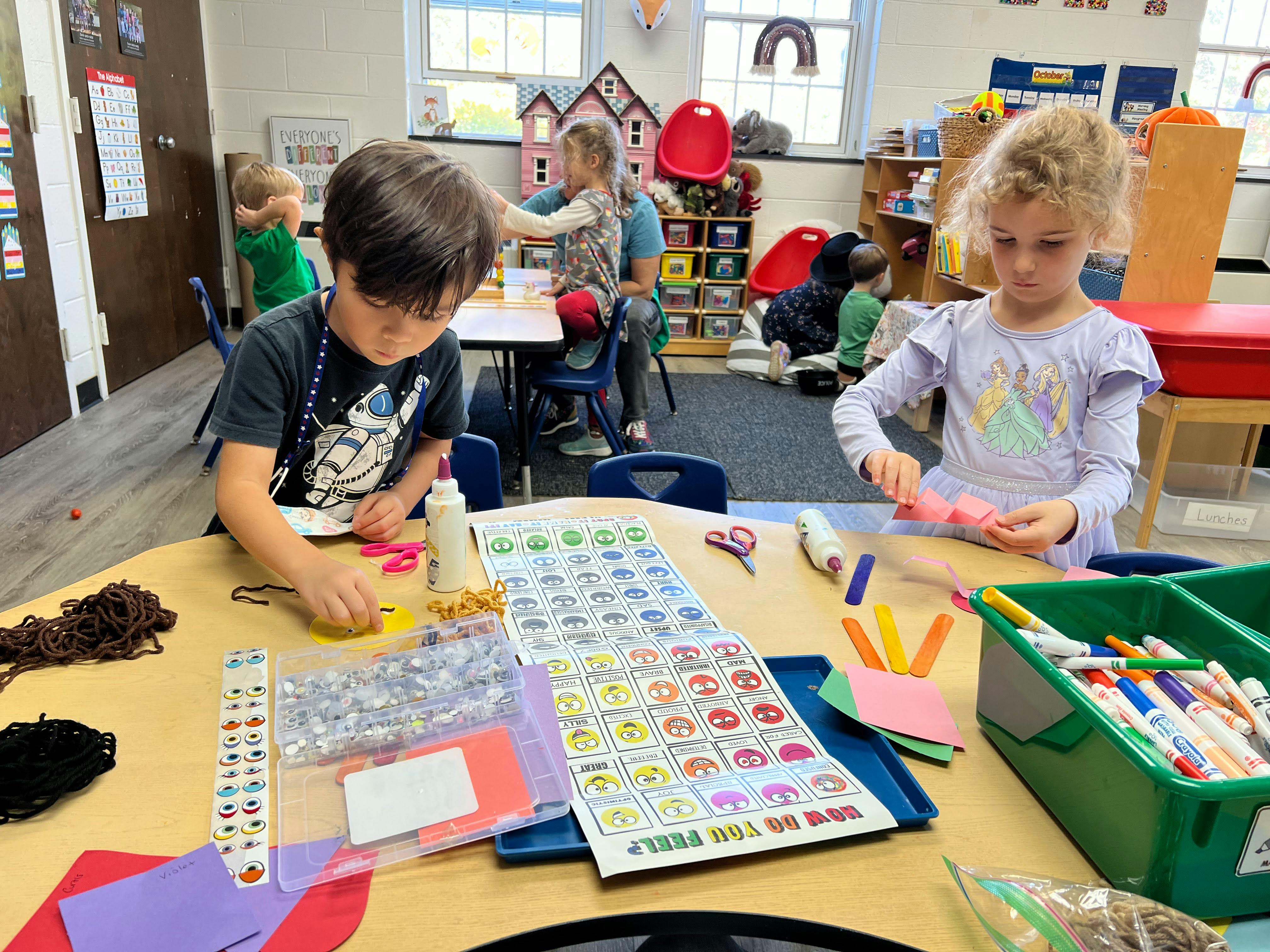 Two children doing crafts at a table in a classroom