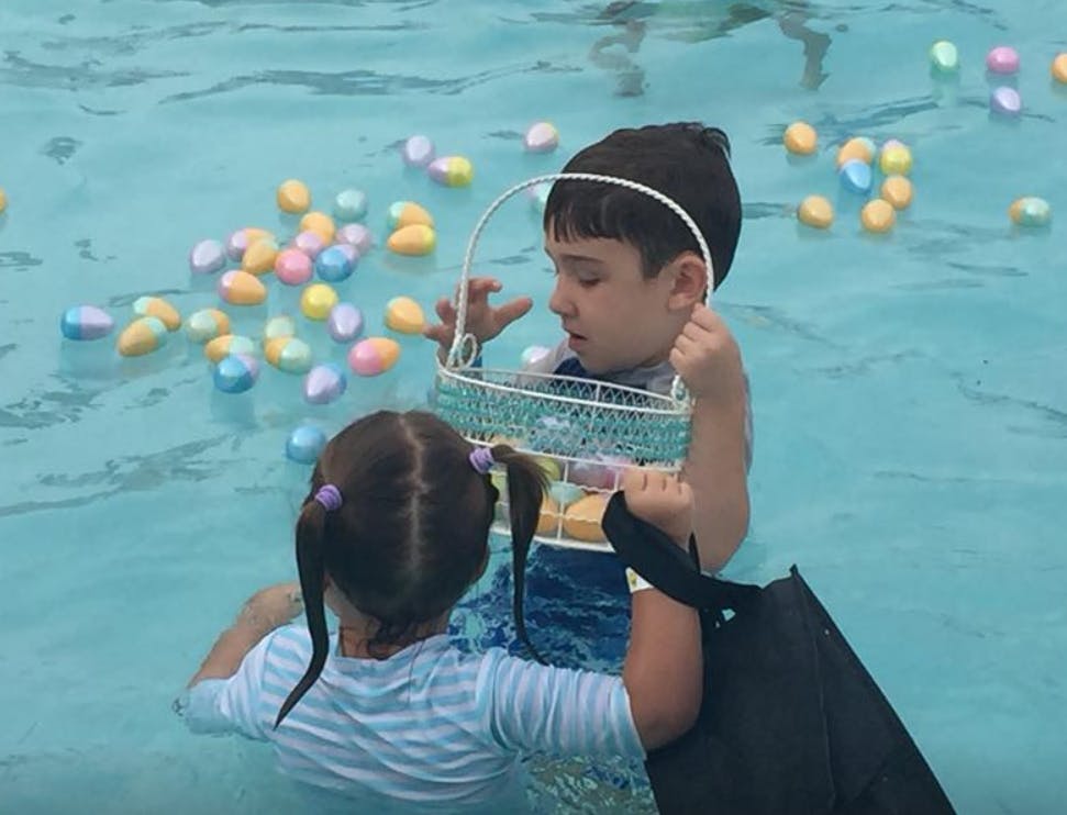 Two children in a pool collecting plastic eggs with baskets