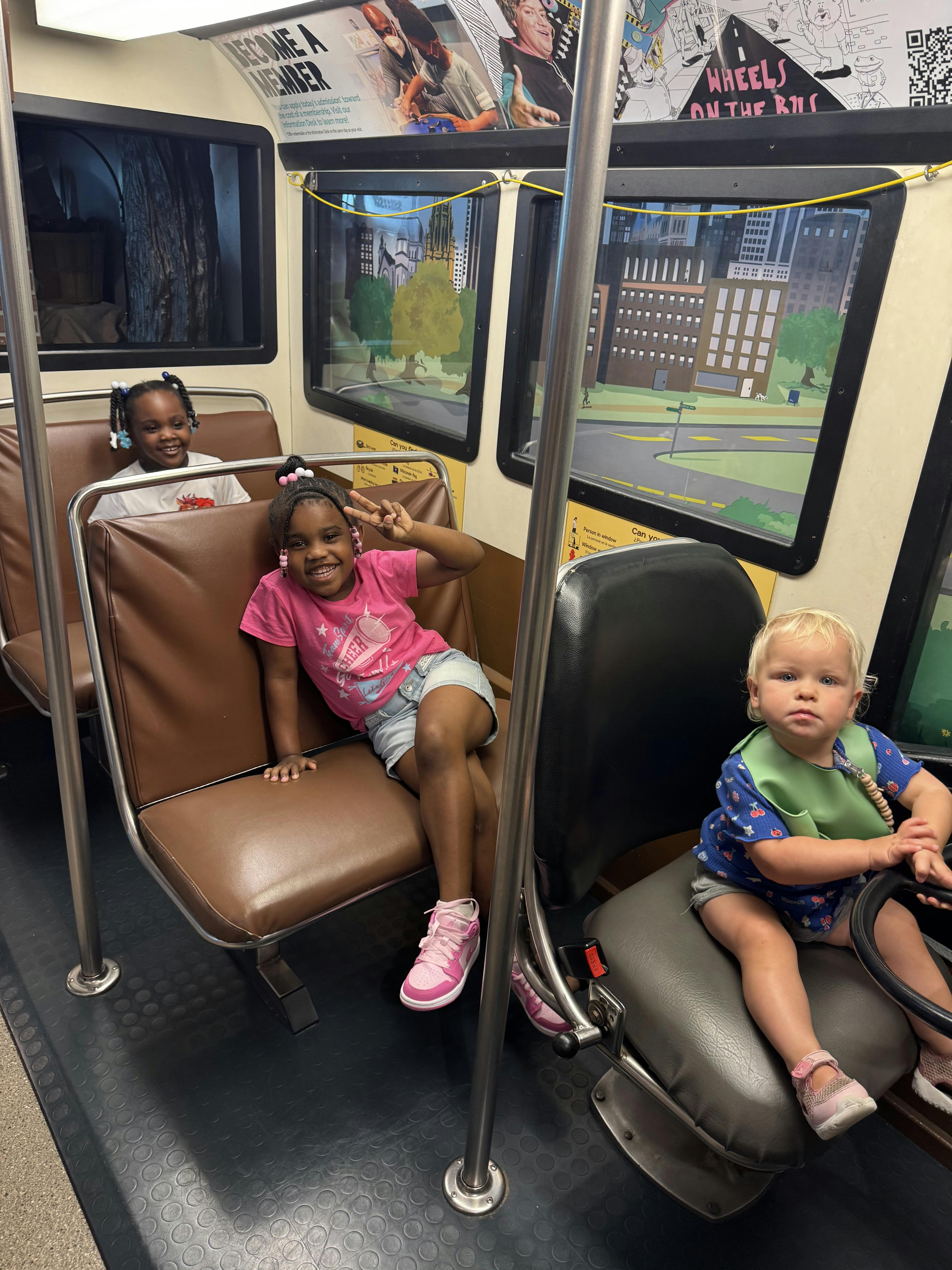 Three children playing on a simulated bus exhibit
