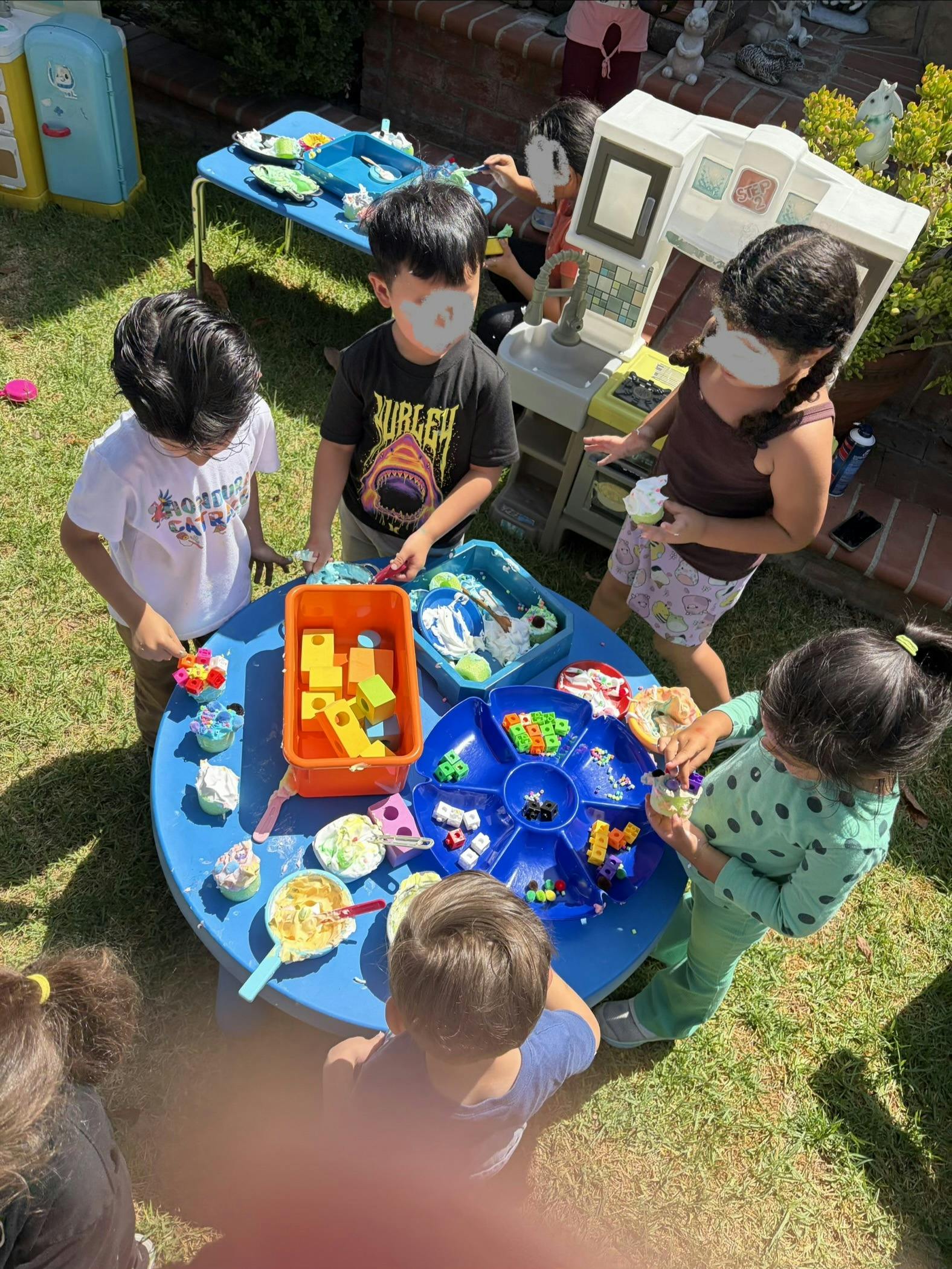 Group of children playing with toys and foam on a table outdoors