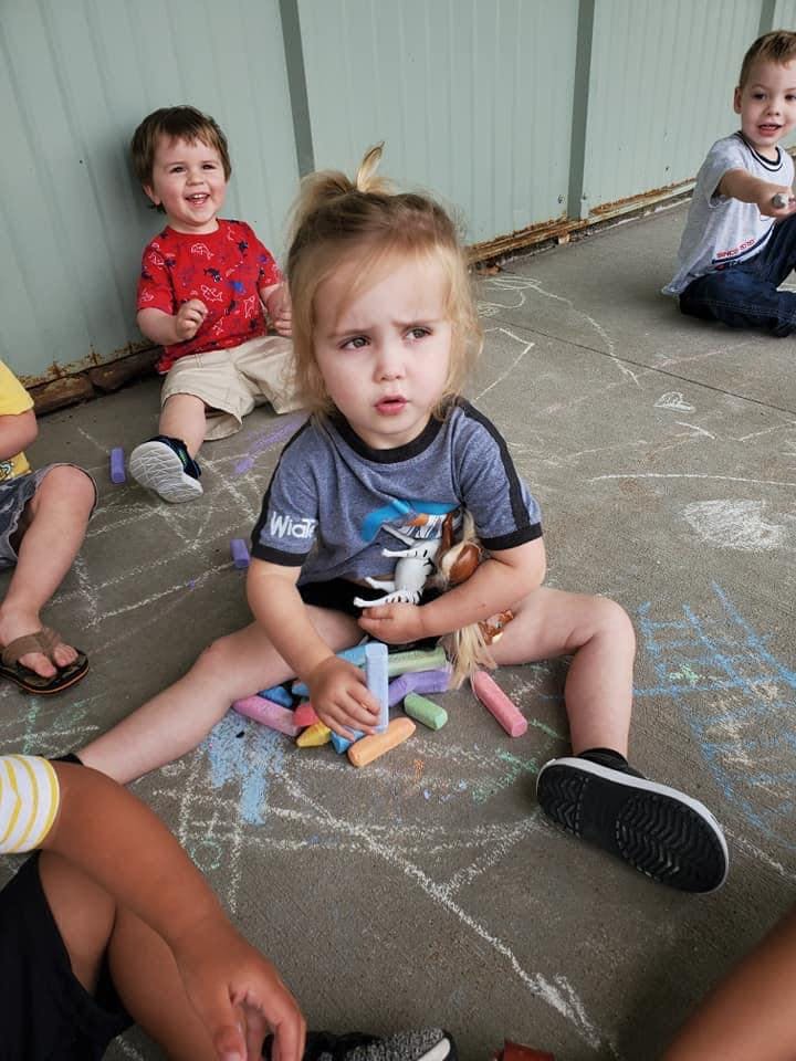 Child sitting on ground with chalk, other children in background