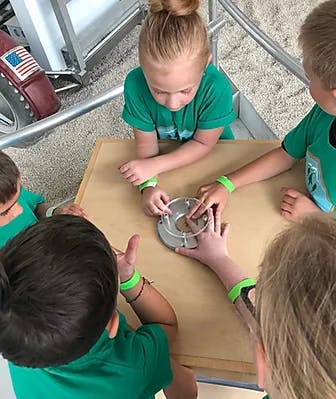 Children gathered around a table, interacting with a circular object
