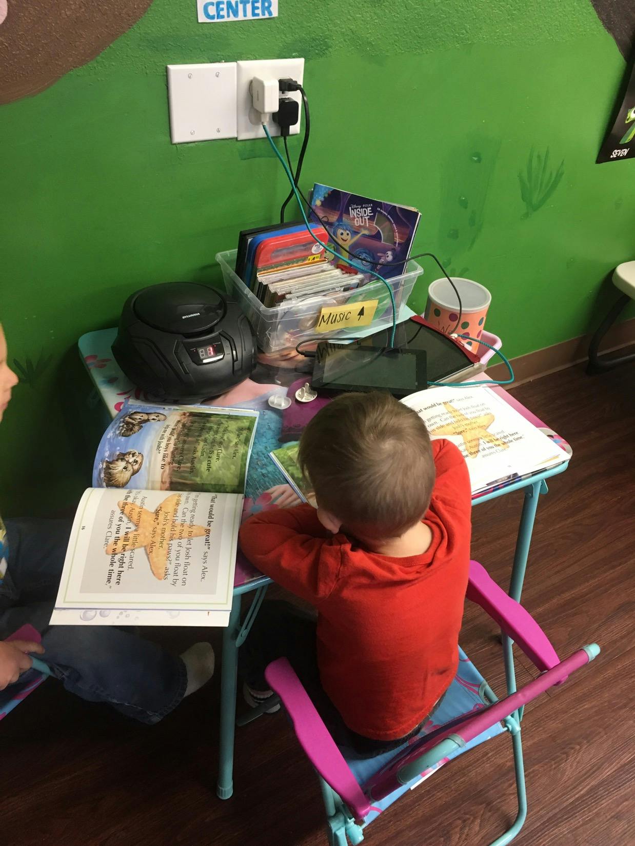 Child in red shirt reading a book at a small table