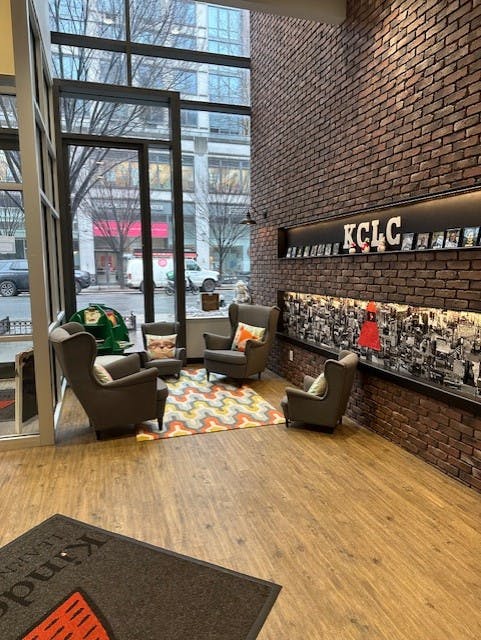 Lobby with brick wall, large windows, four armchairs, and a rug