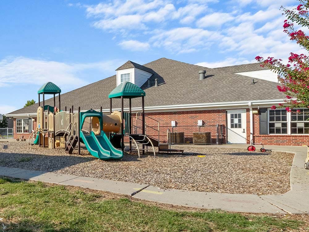 Playground with swings, slides, and climbing structures next to a brick building