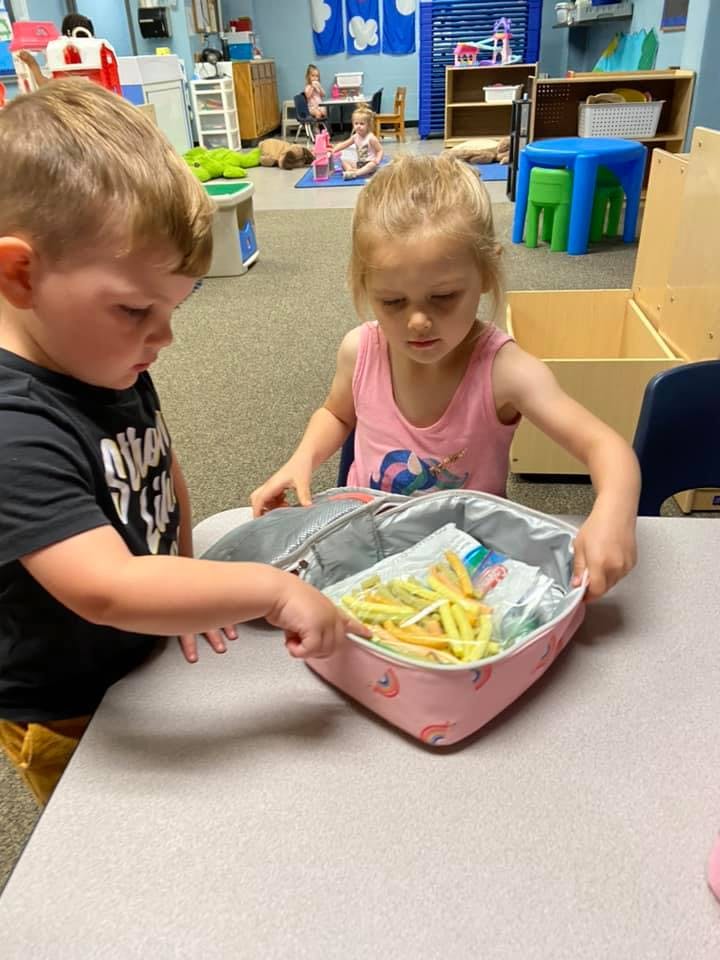 Two children looking into a lunchbox filled with snacks