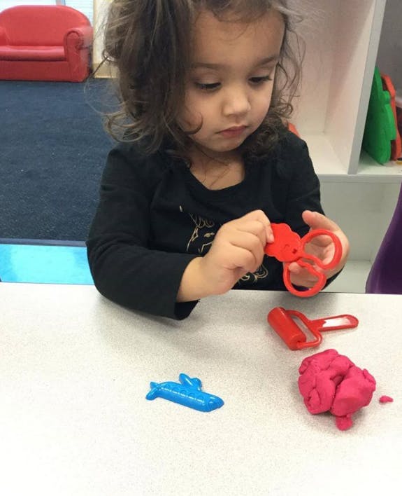 Child playing with red plastic scissors and pink playdough