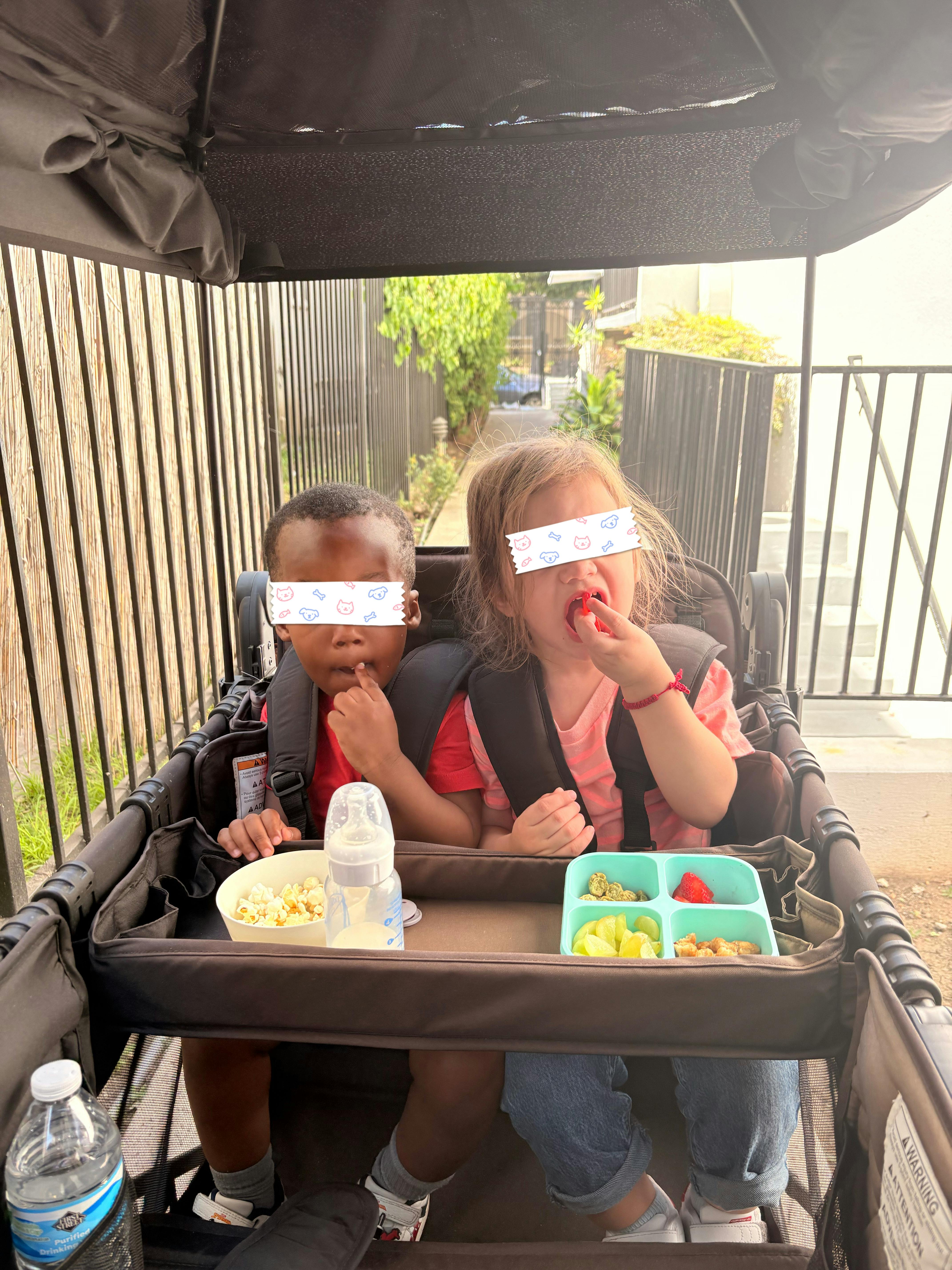 Two children sitting in a stroller eating snacks