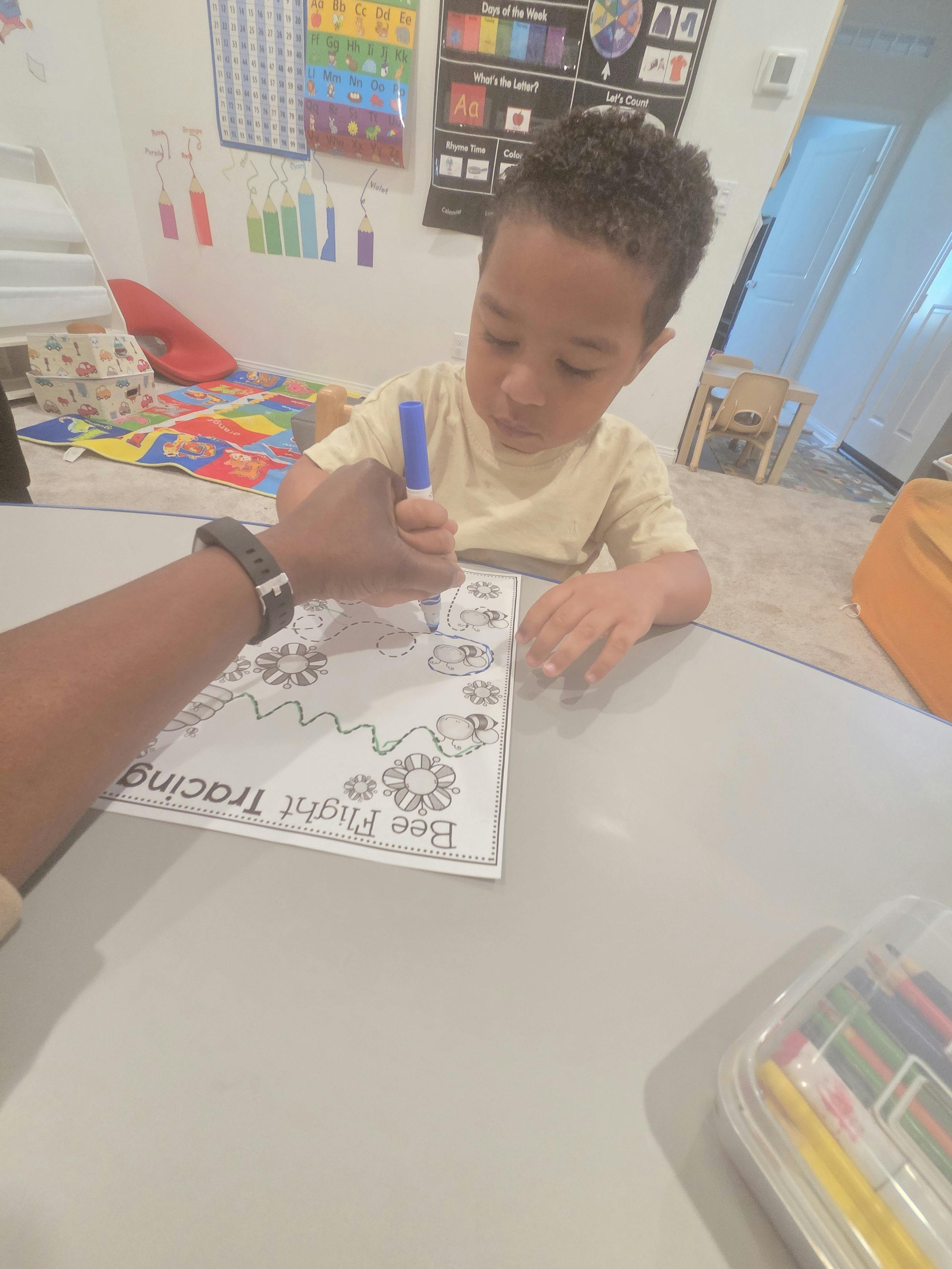 A person guiding a child's hand while tracing lines on a worksheet