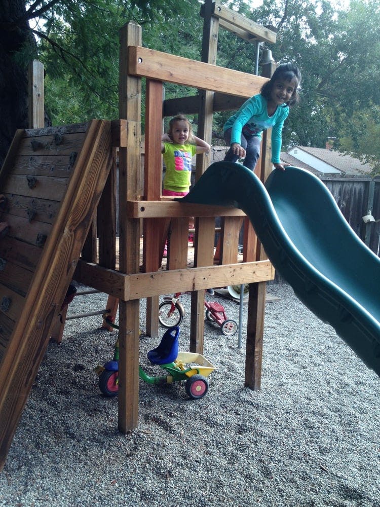Two children on a wooden playground structure with a slide
