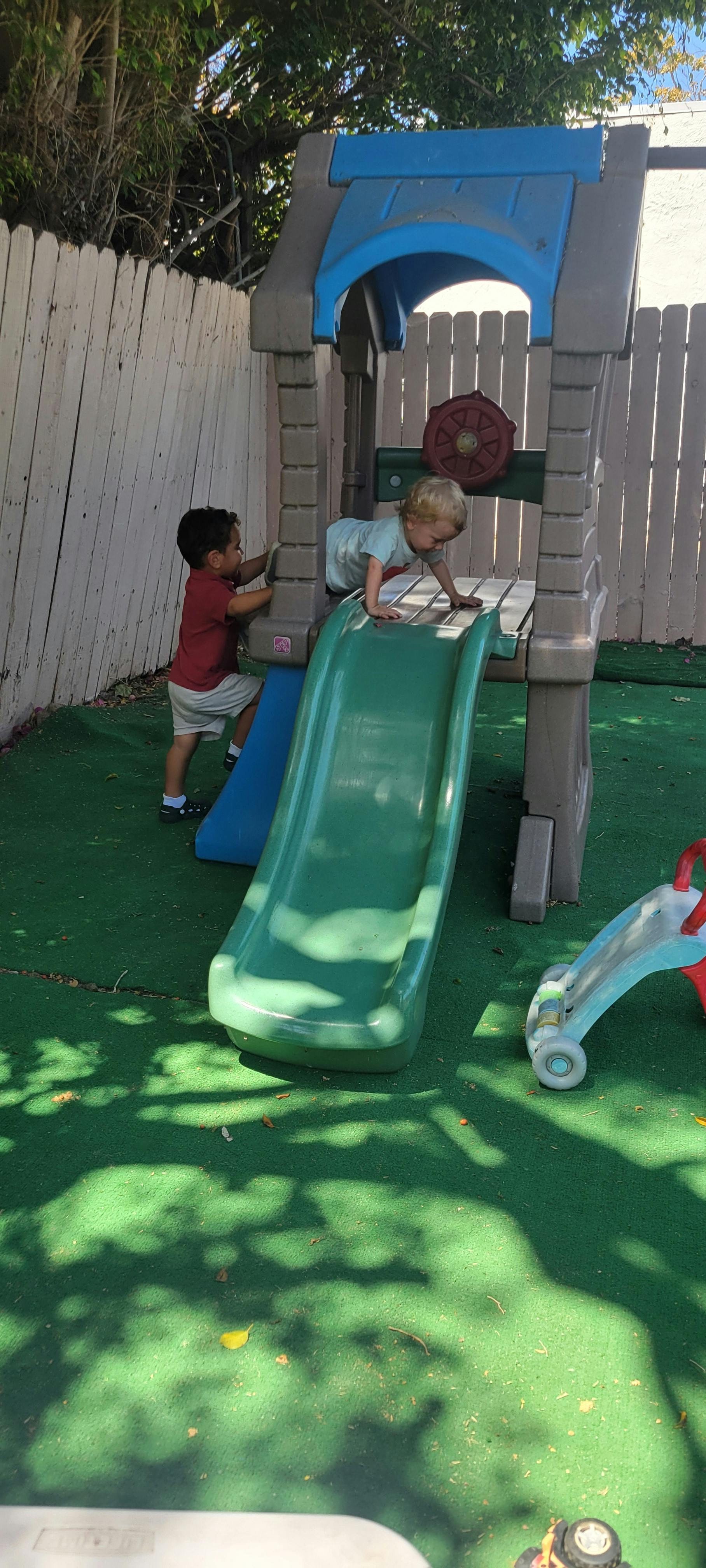 Two children playing on a backyard plastic playground set