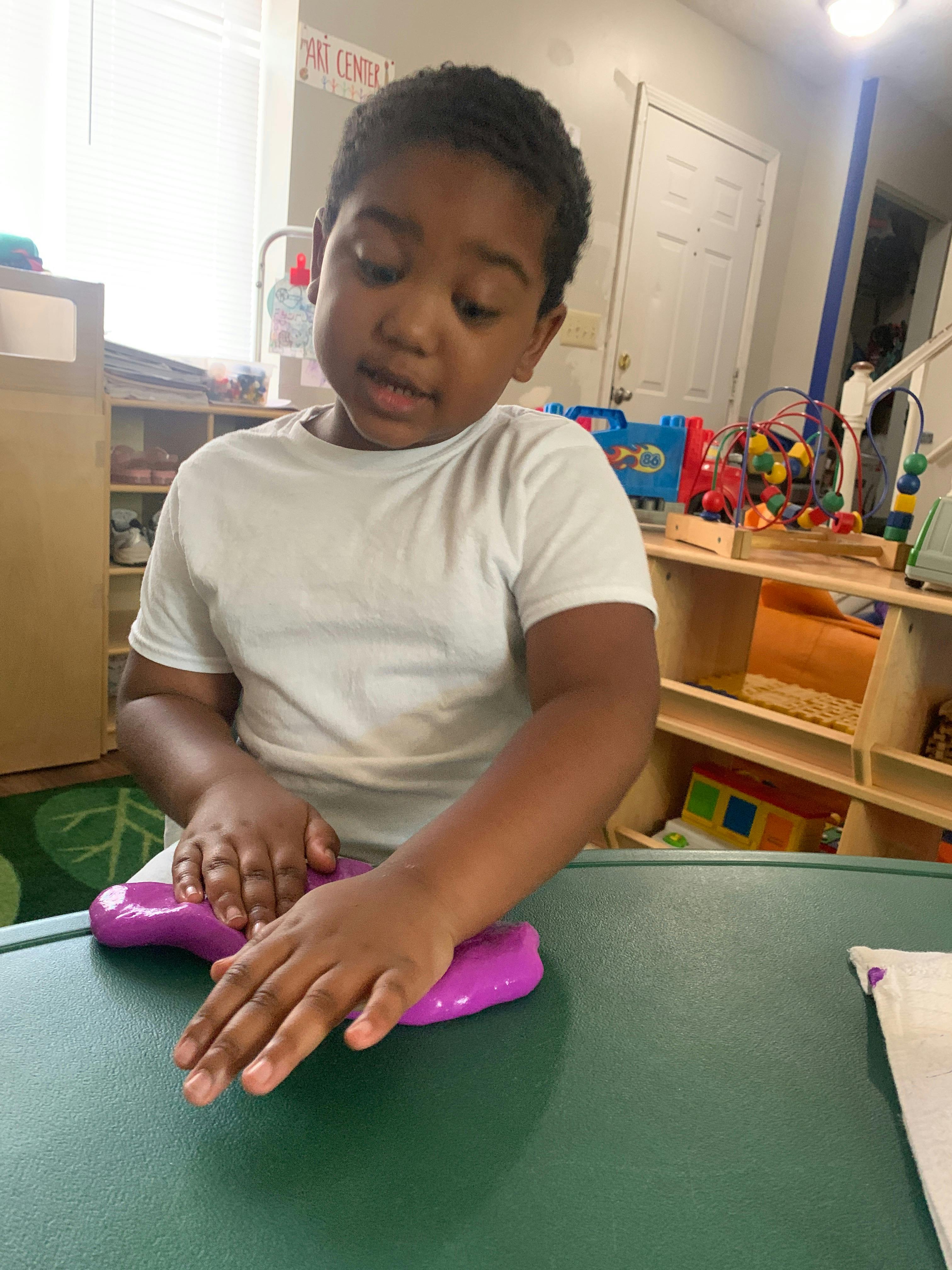 Child playing with purple slime on a green table