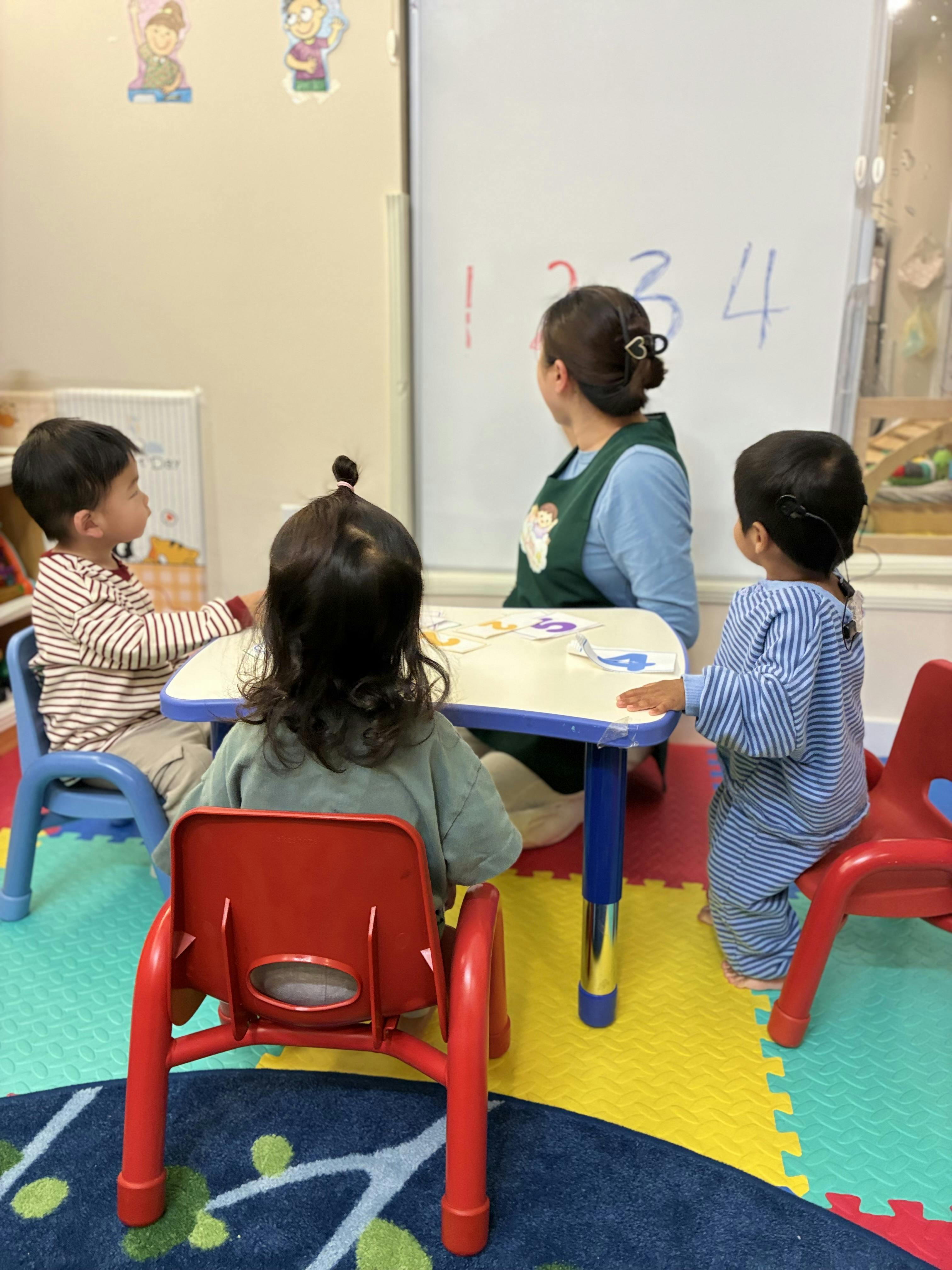Teacher and three children sitting at a table with numbers on a whiteboard