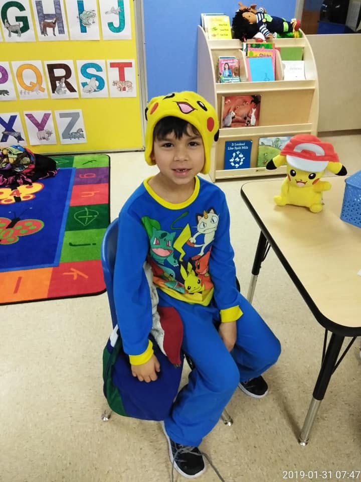 Child in a yellow hat and blue pajamas sitting in a classroom