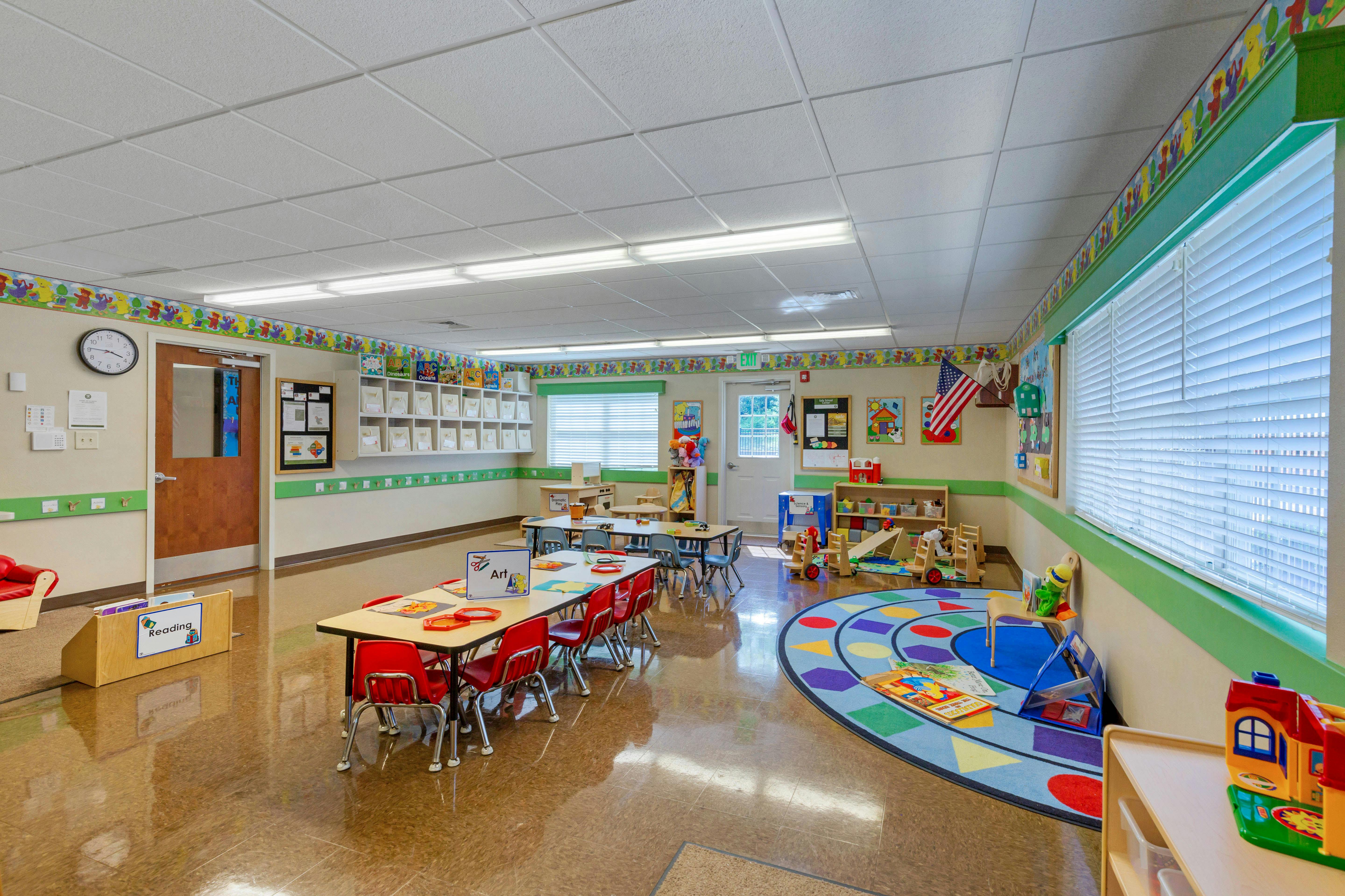 Classroom with child-sized tables and chairs, play area, and reading nook