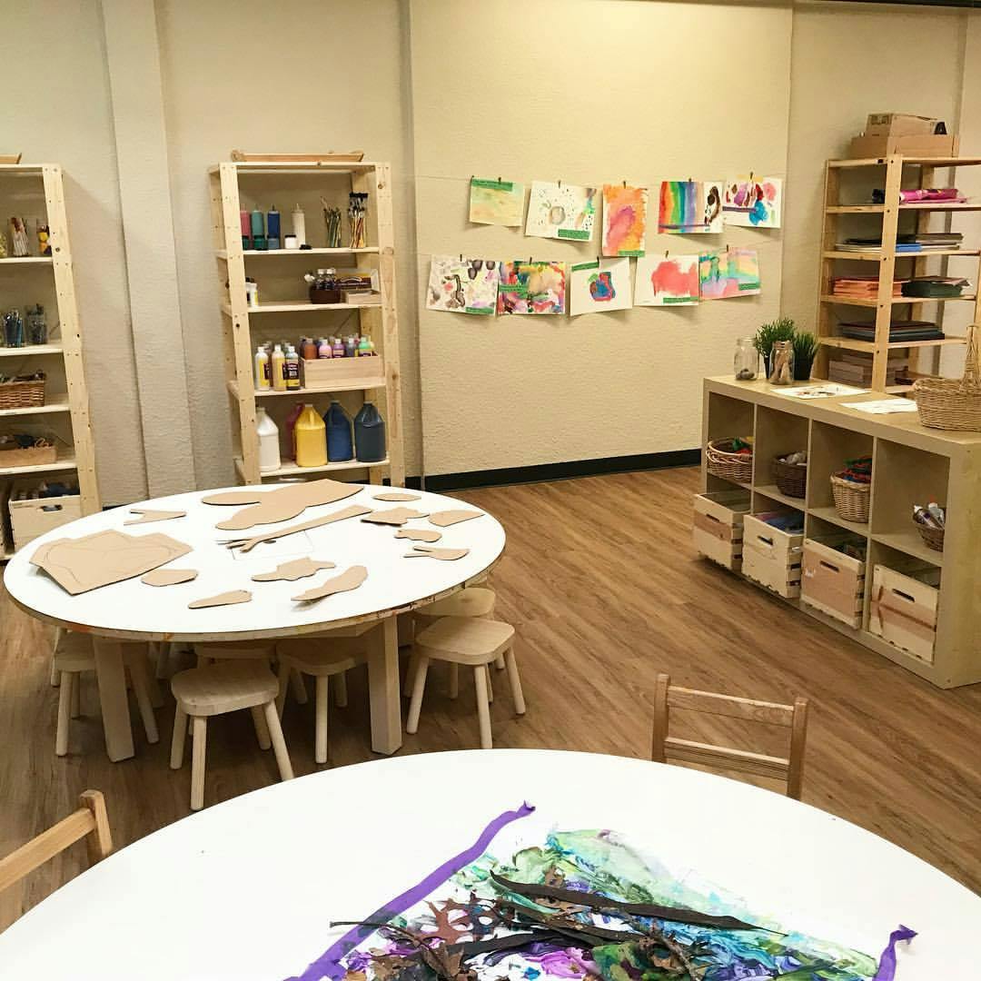 Classroom with tables, shelves, and children's artwork on the wall