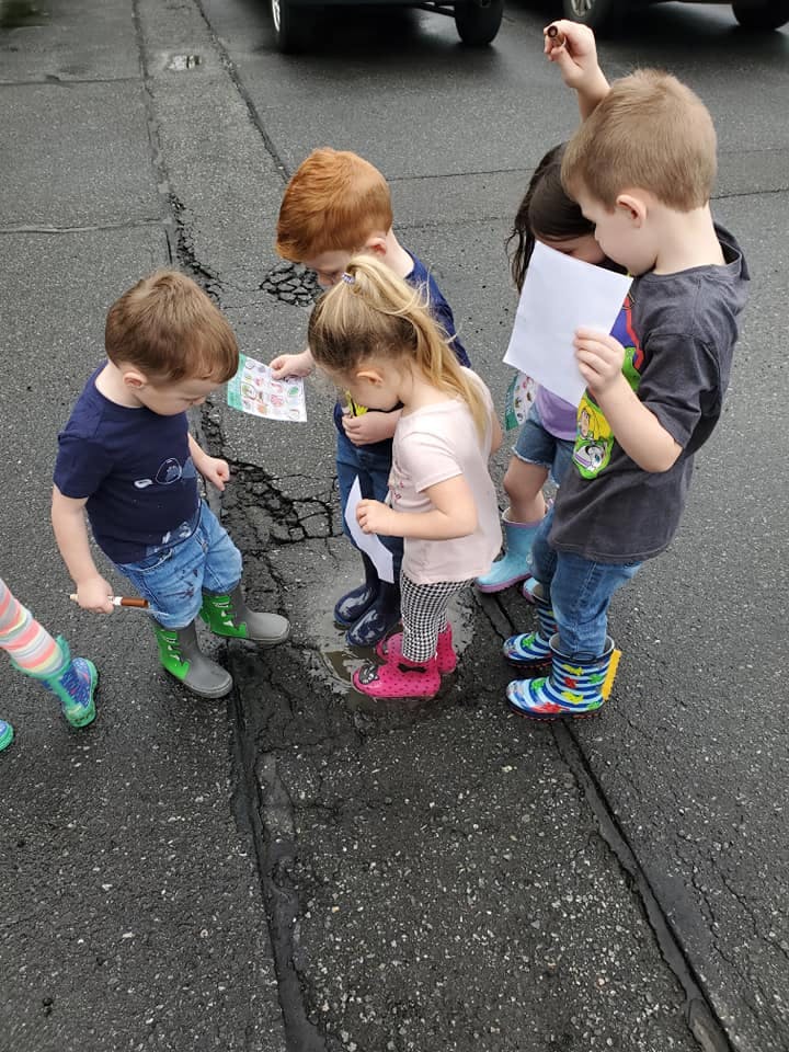 Group of children in rain boots looking at papers on the ground