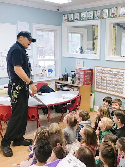 Person in uniform speaking to children sitting on the floor in a classroom