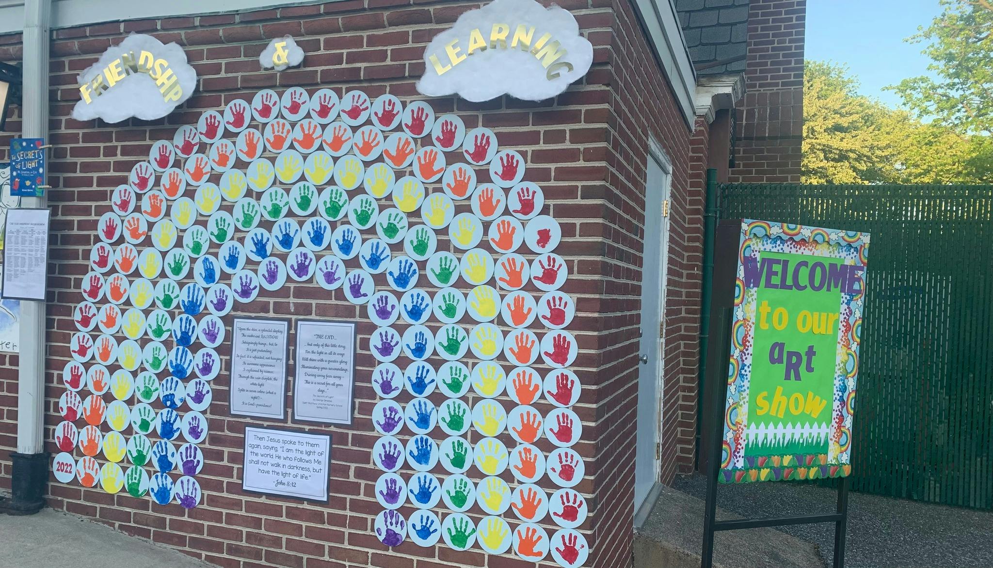 Rainbow made of colorful handprints on a brick wall with a welcome sign