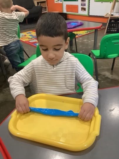 Child playing with blue playdough on a yellow tray