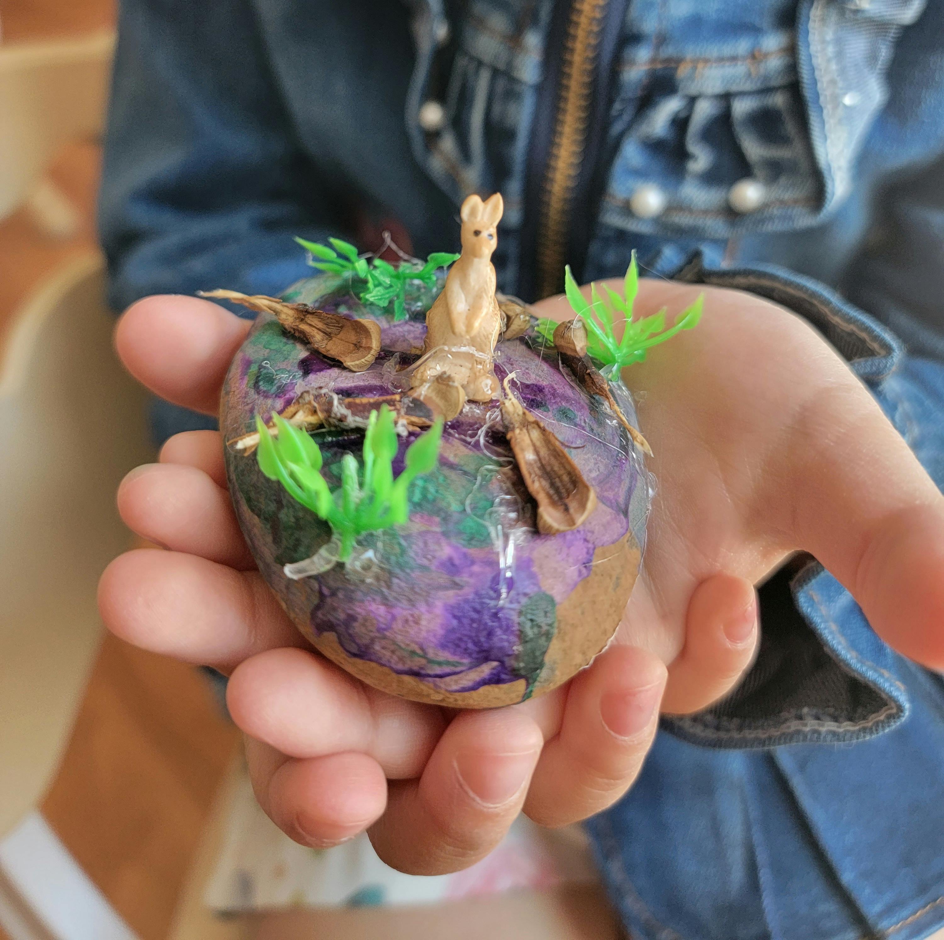 Child holding a decorated rock with a small animal figurine and plastic plants