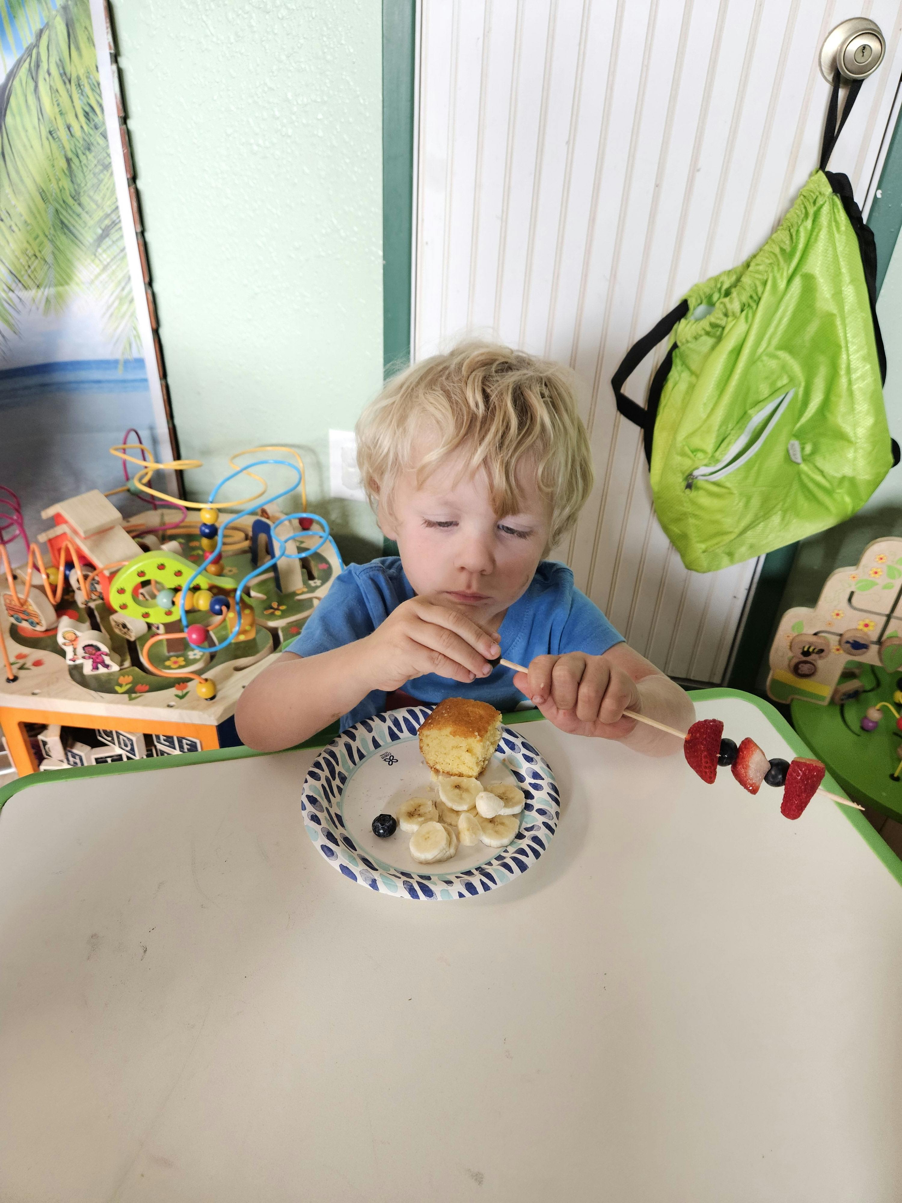 Child eating from a plate with a fruit skewer
