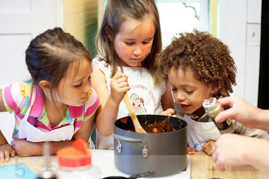 Three children cooking with a pot and spoon