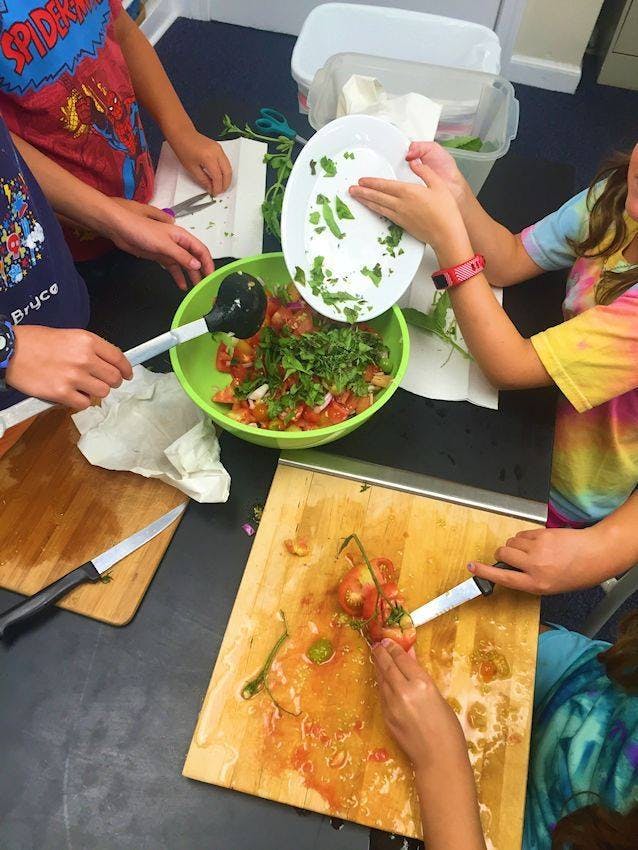 Children preparing food, chopping vegetables and adding ingredients to a bowl