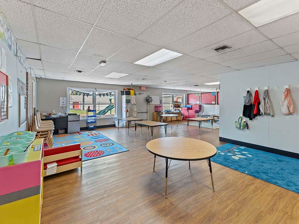 Classroom with tables, colorful rugs, and jackets hanging on a wall