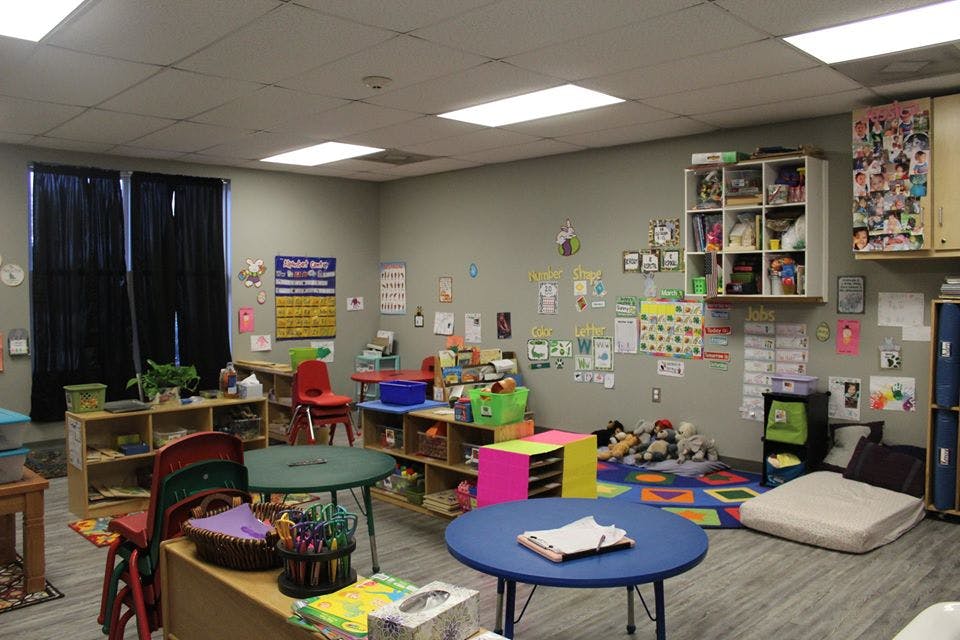 Classroom with small tables, chairs, shelves, and decorations on the walls