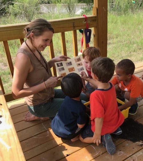 Person showing a book to three children outdoors